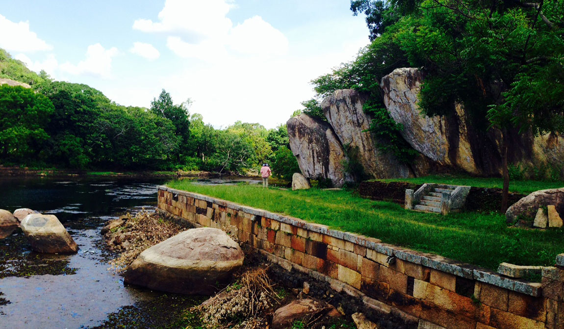 A picturesque river scene with lush greenery and dramatic rock outcrops, showcasing the natural beauty of the Sigiriya area.