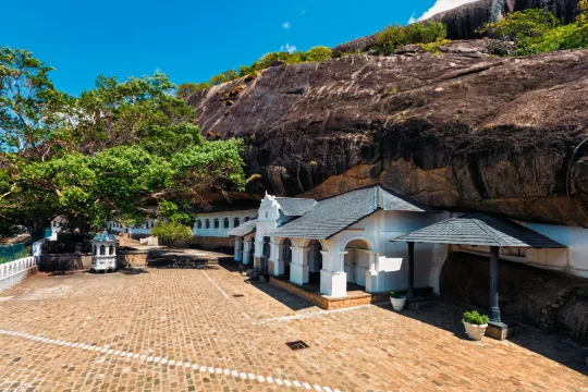 The serene Dambulla Cave Temple complex, nestled against a majestic rock face, offering a peaceful retreat near Sigiri Vananthara, a nature resort in Sigiriya.